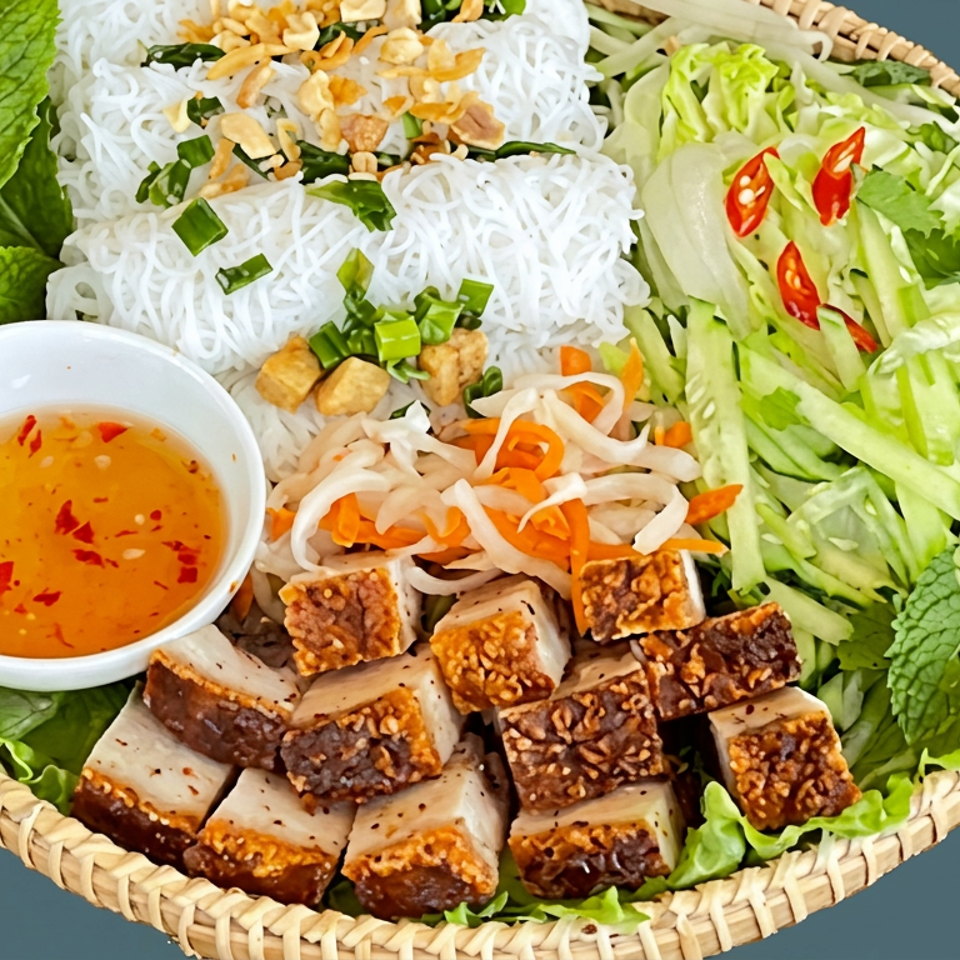 Vietnamese noodle bowl with crispy pork, fresh herbs, cucumber, lettuce, pickled vegetables, peanuts, and chili dipping sauce.